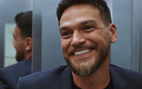 O ator Emilio Dantas sorri forçadamente em cena da novela Vai na Fé como o personagem Theo