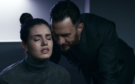 Camila Queiroz e Gabriel Braga Nunes em cena de Verdades Secretas 2:atriz está sentada de olhos fechados enquanto ator conversa com ela ao pé do ouvido