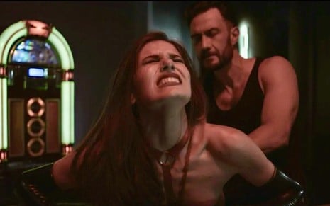 Camila Queiroz e Gabriel Braga Nunes em cena de Verdades Secretas 2:atriz está sentada de olhos fechados enquanto ator a segura por trás