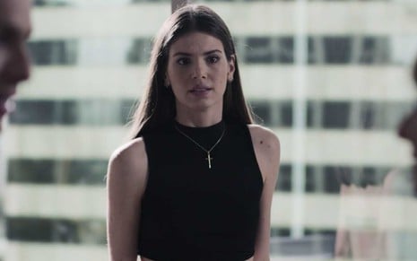 A atriz Camila Queiroz caracterizada como Angel  em uma sala de reunião envidraçada com prédios ao fundo em cena de Verdades Secretas 2