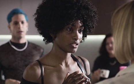 Erika Januza em cena de Verdades Secretas 2: atriz está caracterizada como Laila, usa regata branca, cabelo afro e olha com atenção para alguém fora do quadro