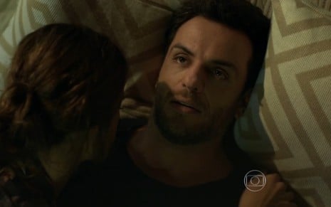 Rodrigo Lombardi grava deitado, com camiseta preta e olhar triste e vazio como Alex de Verdades Secretas