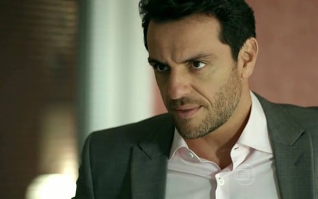 O ator Rodrigo Lombardi, de camisa e terno, com expressão séria em cena de Verdades Secretas