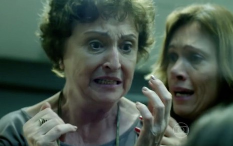 Ana Lucia Torre levanta as mãos e faz cara de pânico enquanto é amparada por Bel Kutner em cena de Verdades Secretas