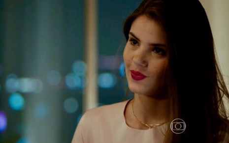 A atriz Camila Queiroz usa batom vermelho e roupa clara ao fazer um olhar de vitória durante gravação de cena de Verdades Secretas, como Angel