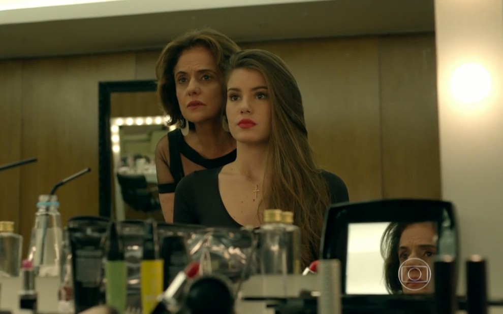 Camila Queiroz grava com batom vermelho olhando para Marieta Severo através do espelho, como Angel e Fanny de Verdades Secretas