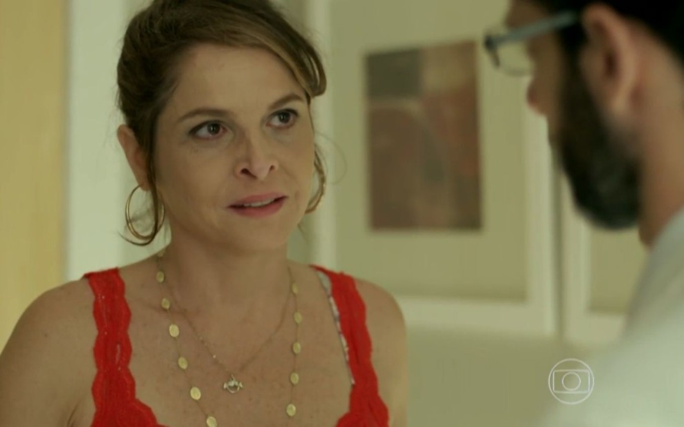 Drica Moraes grava cena com expressão tensa, de cabelo preso e regata vermelha, como Carolina em Verdades Secretas, da Globo