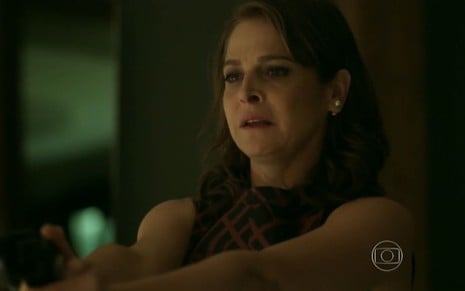 Drica Moraes grava cena com expressão tensa e segurando uma arma, como Carolina em Verdades Secretas, da Globo