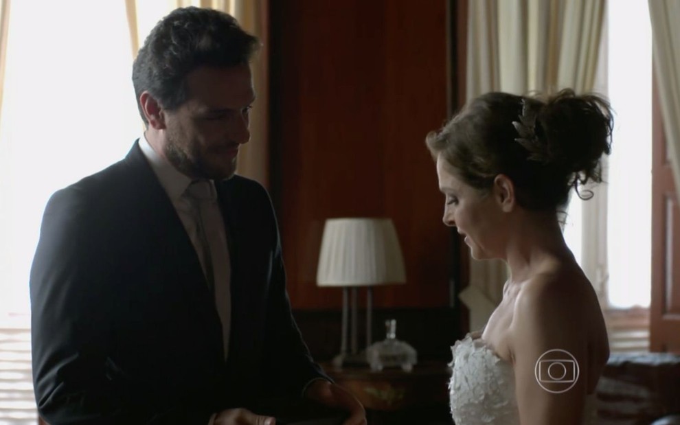 Foto dos personagens Alex (Rodrigo Lombardi) e Carolina (Drica Moraes) em cena de Verdades Secretas, da Globo, em que ele aparece de terno e ela vestida de noiva