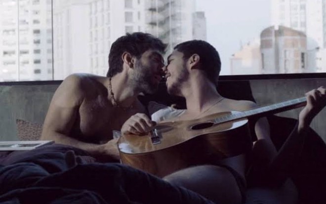 Sentados na cama, Benji (Rodrigo Pandolfo) beija Bruno (João Vitor Silva) em cena de Verdades Secretas 2