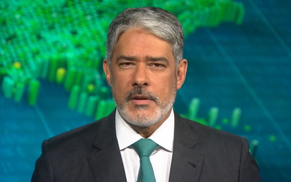 William Bonner usa terno preto, camisa branca e gravata verde enquanto apresenta o Jornal Nacional na Globo