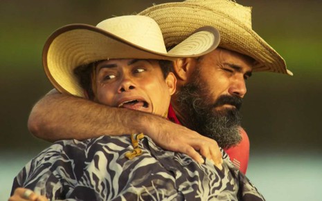 Ator Silvero Pereira olha para o lado com cara de pavor enquanto é abraçado por Juliano Cazarré em Pantanal