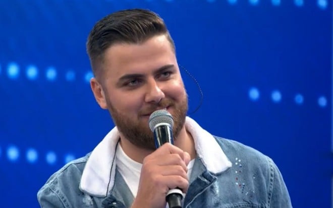 Sorridente, Zé Neto segura o microfone enquanto fala no palco do Domingão com Huck