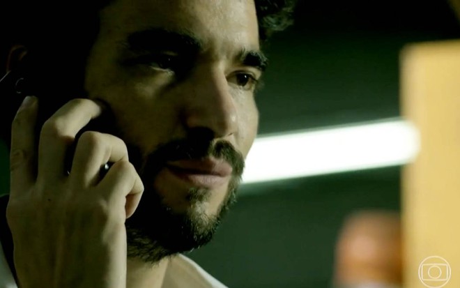 Ator Caio Blat olha para frente com cara de sério e segura telefone em cena de Império