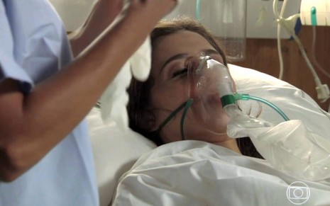 Atriz Marjorie Estiano surge deitada em cama de hospital, com um aparelho para respirara, em cena da novela Império