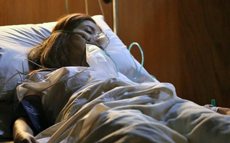Atriz Marjorie Estiano surge deitada em cama de hospital, com um aparelho para respirar, em cena da novela Império