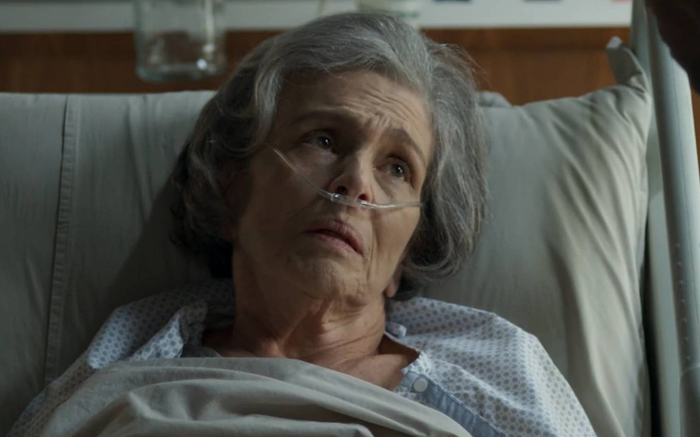 Atriz Irene Ravache surge deitada em cama de hospital enquanto olha para cima em cena da novela Pega Pega