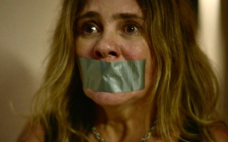 A atriz Adriana Esteves está com fita adesiva na boca e em close em cena da série Os Outros, do Globoplay