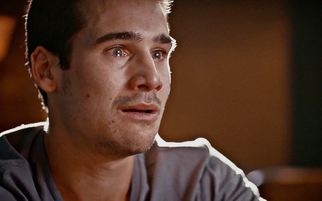 O ator Nicolas Prattes está em close e com lágrimas nos olhos em cena da novela Todas as Flores
