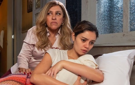 Zoé (Regina Casé) está sentada na cama de Maíra (Sophie Charlotte), que segura um bebê nos braços em cena de Todas as Flores