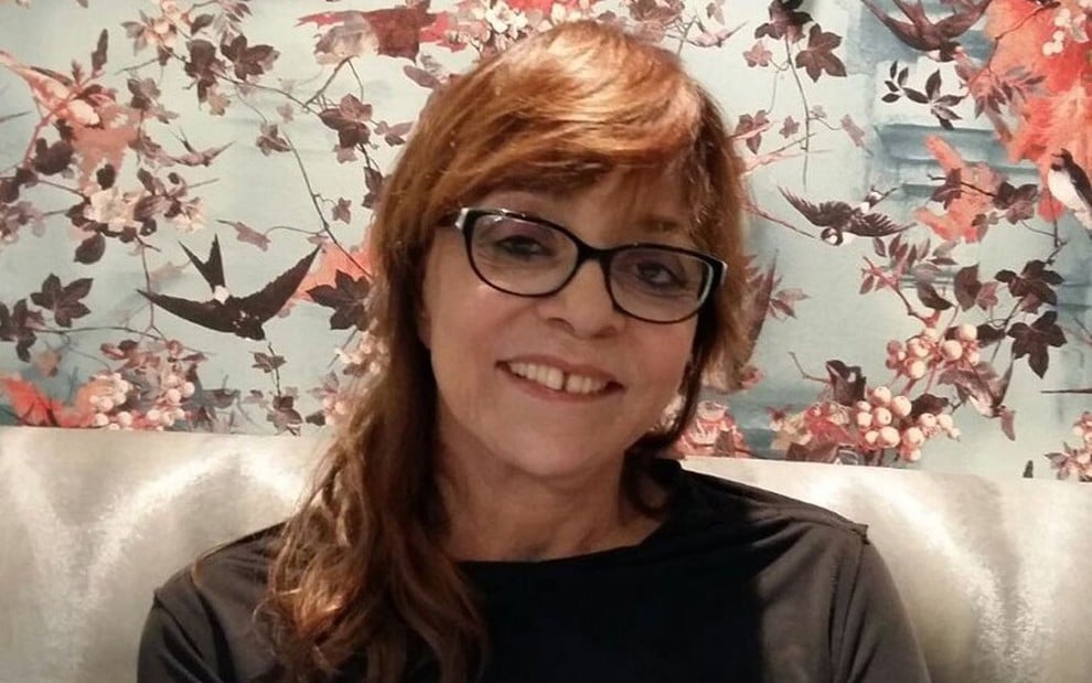 A autora de novelas Gloria Perez; ela está de óculos, sentada, posando para a foto e sorrindo