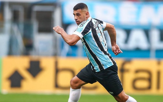 Diego Souza correndo em jogo na Arena do Grêmio; ele está com o uniforme tradicional do clube