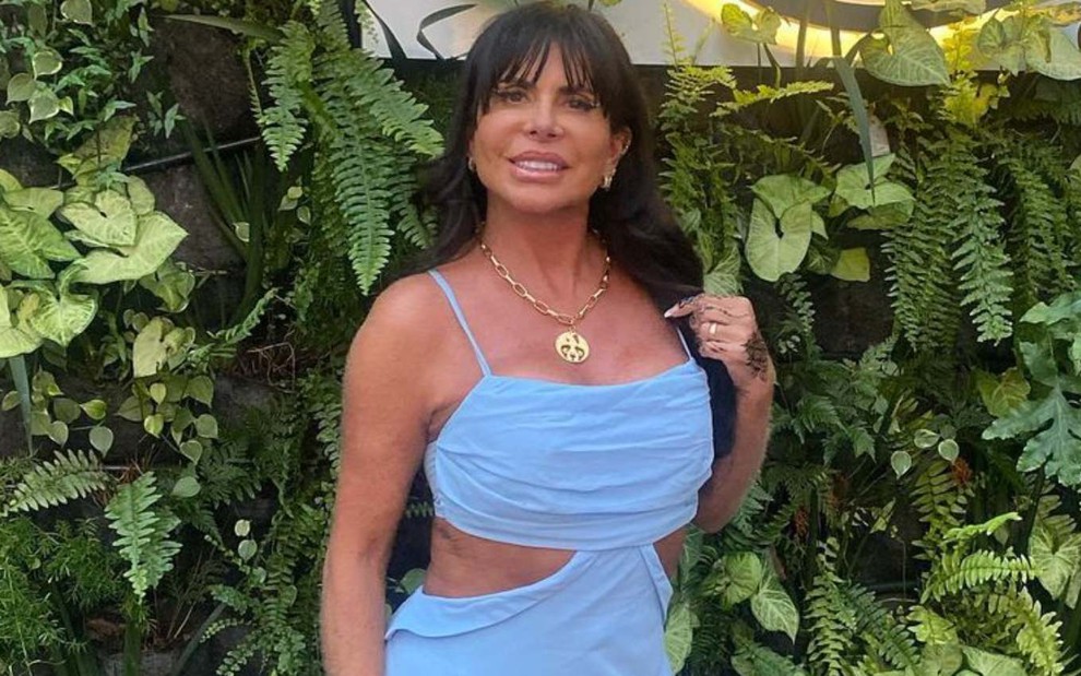 Gretchen Miranda em foto publicada no Instagram, sorrindo, de vestido azul, em frente a parede com folhas