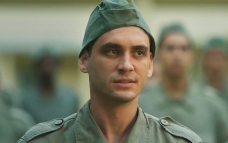 Guilherme Prates com roupa verde de soldado em cena como Lorenzo na novela Além da Ilusão
