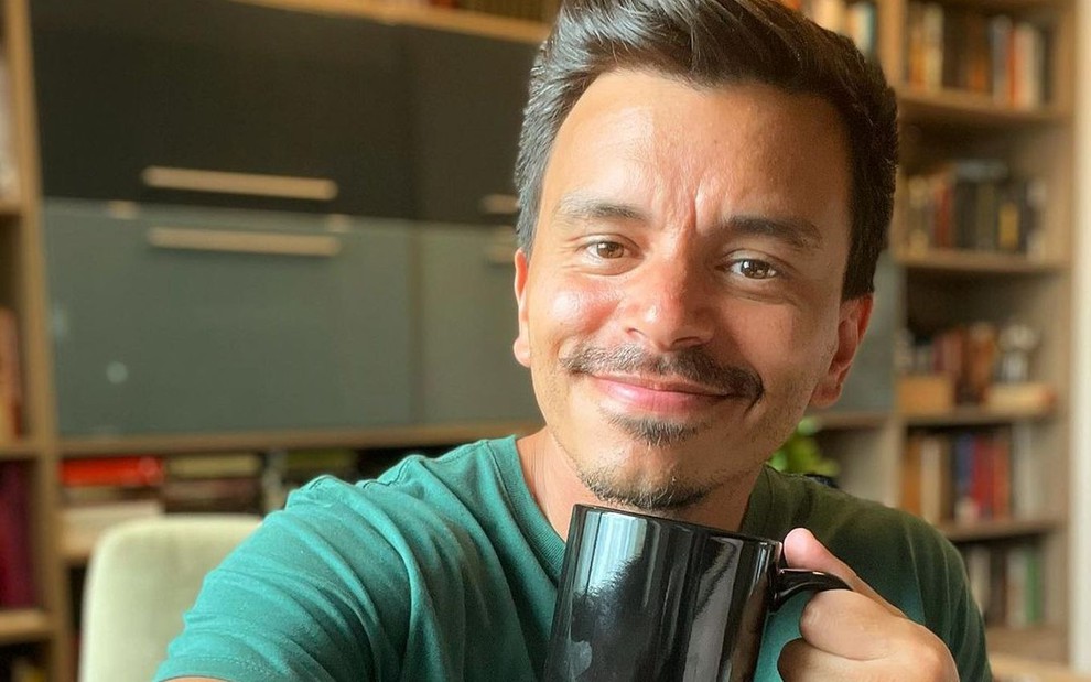 Gustavo Reiz está posando para a foto com uma caneca preta