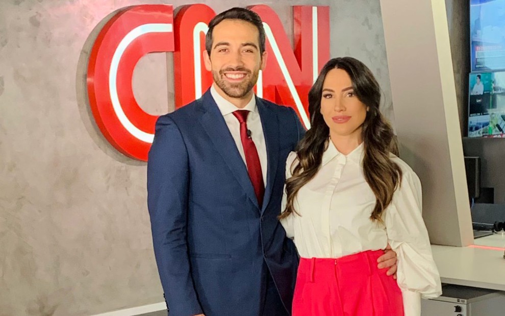 O comentarista Gustavo Uribe e a repórter Tainá Falcão posam à frente da logomarca da CNN Brasil, em Brasília