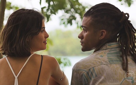 Os atores Julia Dalavia e Lucas Leto como Marcelo e Guta em Pantanal; eles estão lado a lado em uma paisagem de natureza