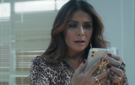 Em cena de Travessia, Giovanna Antonelli está olhando algo na tela do celular com a expressão de surpresa
