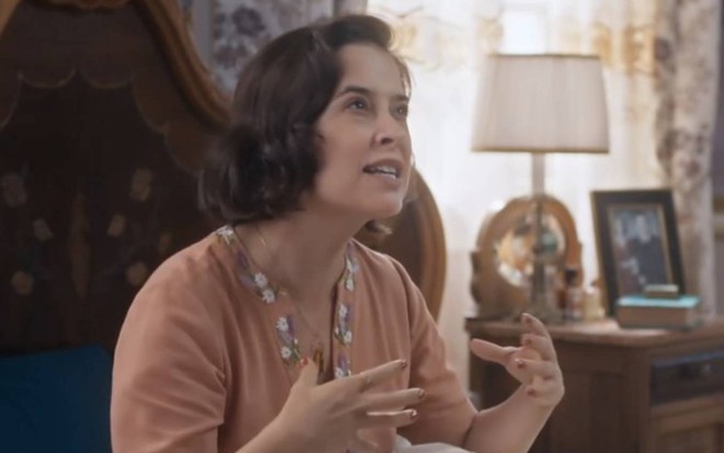 A atriz Paloma Duarte está caracterizada como sua personagem de Além da Ilusão; ela sentada e gesticulando