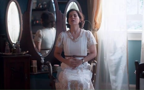 A atriz Paloma Duarte como Heloísa em Além da Ilusão; ela está sentada sentindo dores na região abdominal