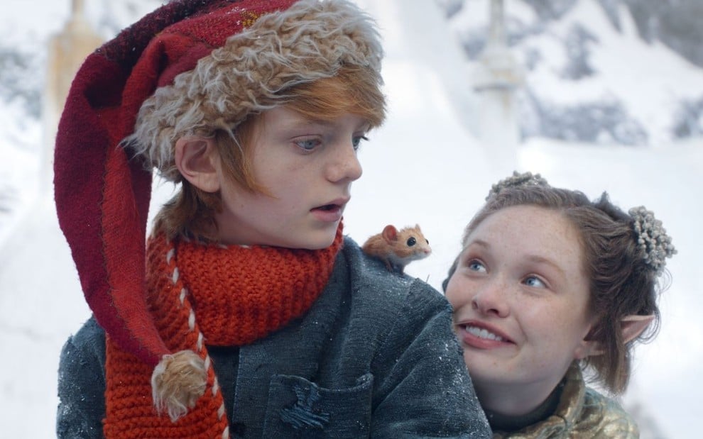 Em um cenário com neve, Henry Lawfull e Zoe Margaret Colletti conversam em cena do filme Um Menino Chamado Natal