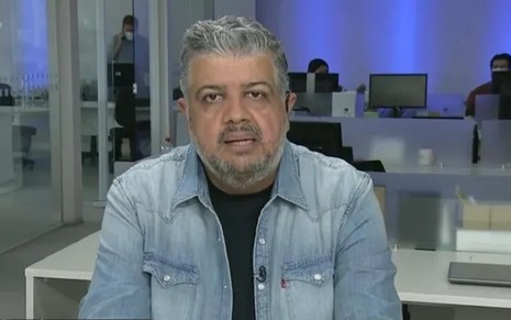 Héverton Guimarães com uma jaqueta jeans, camisa preta e falando sério no Jogo Aberto