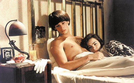 Os atores Rodrigo Santoro e Ana Paula Arósio como Malthus e Hilda em Hilda Furacão; eles estão deitados na cama enquanto ele olha para baixo e ela o abraça, ambos com cara de desanimados