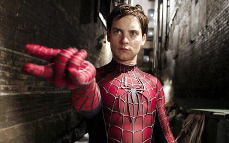 Tobey Maguire interpretando Peter Parker, o Homem-Aranha. Ele usa a fantasia clássica e faz uma pose para soltar a teia de aranha