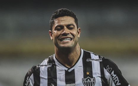 Jogador Hulk, do Atlético Mineiro, com uma camisa preta e branca e sorrindo para a câmera após fazer um gol