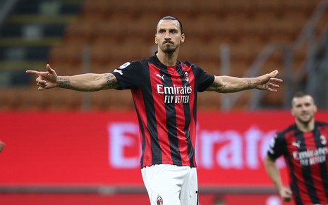 Atacante sueco Ibrahimovic, usando a camisa vermelha e preta do MIlan, abre os braços para comemorar um gol feito no Campeonato Italiano