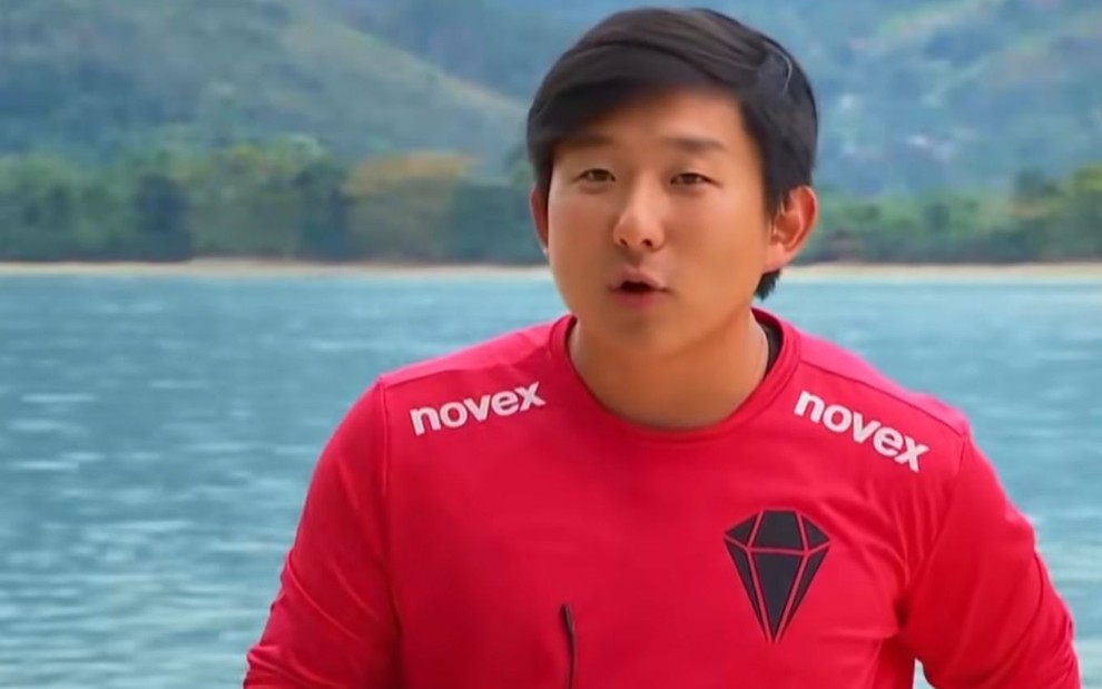 O hipnólogo Pyong Lee no Ilha Record de camiseta vermelha, em frente à praia, no reality Ilha Record