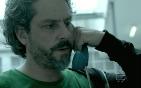 O ator Alexandre Nero segurando telefone, com expressão séria e confusa em cena de Império