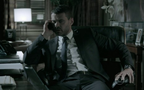 O ator Carmo Dalla Vecchia de terno e gravata, falando ao telefone com expressão séria, em cena de Império