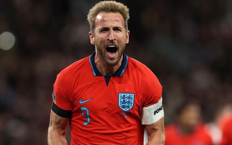 Harry Kane, da Inglaterra, comemora gol e veste uniforme vermelho com detalhes azuis