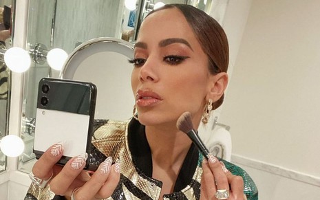 Anitta passa maquiagem no rosto enquanto se olha em celular dobrável em foto de seu Instagram