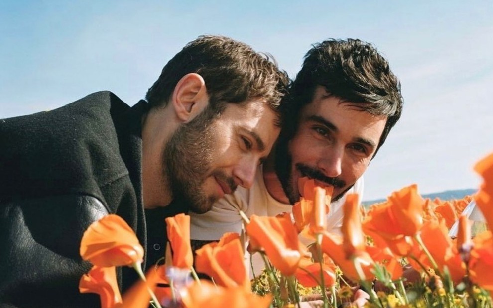 O ator Julian Morris com seu parceiro Landon Ross em foto publicada no Instagram; eles aparecem abraçados em um campo de flores laranjas