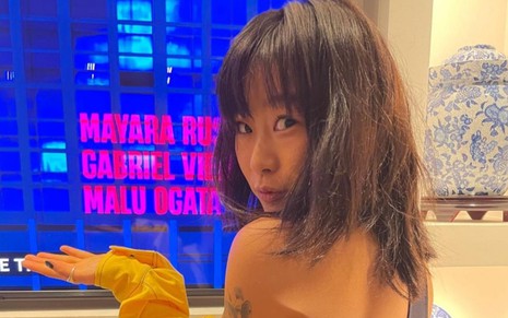 A atriz Malu Ogata em foto publicada no Instagram em que aparece sorrindo na frente de uma TV que mostra os créditos com seu nome na novela Verdades Secretas 2, da Globo