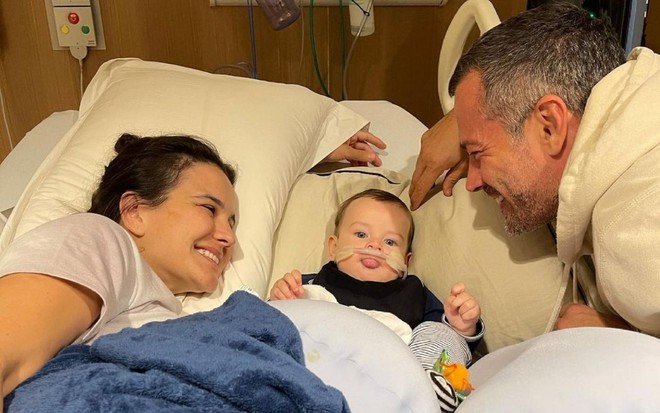 Foto de Kyra Gracie, o filho Rayan e Malvino Salvador deitados em uma cama de hospital
