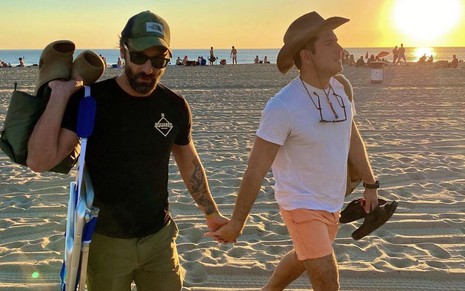 Foto do casal Marco Calvani e Marco Pigossi andando de mãos dadas na praia em foto do Instagram do diretor