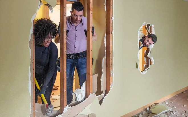 Integrantes do Irmãos à Obra quebram a casa de uma participante. Eles estão dentro do buraco e a moça, toda de preto, tem uma marreta na mão.